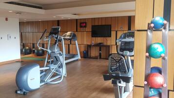 Un gimnasio con máquinas de cardio, televisión y pelotas de ejercicio.
