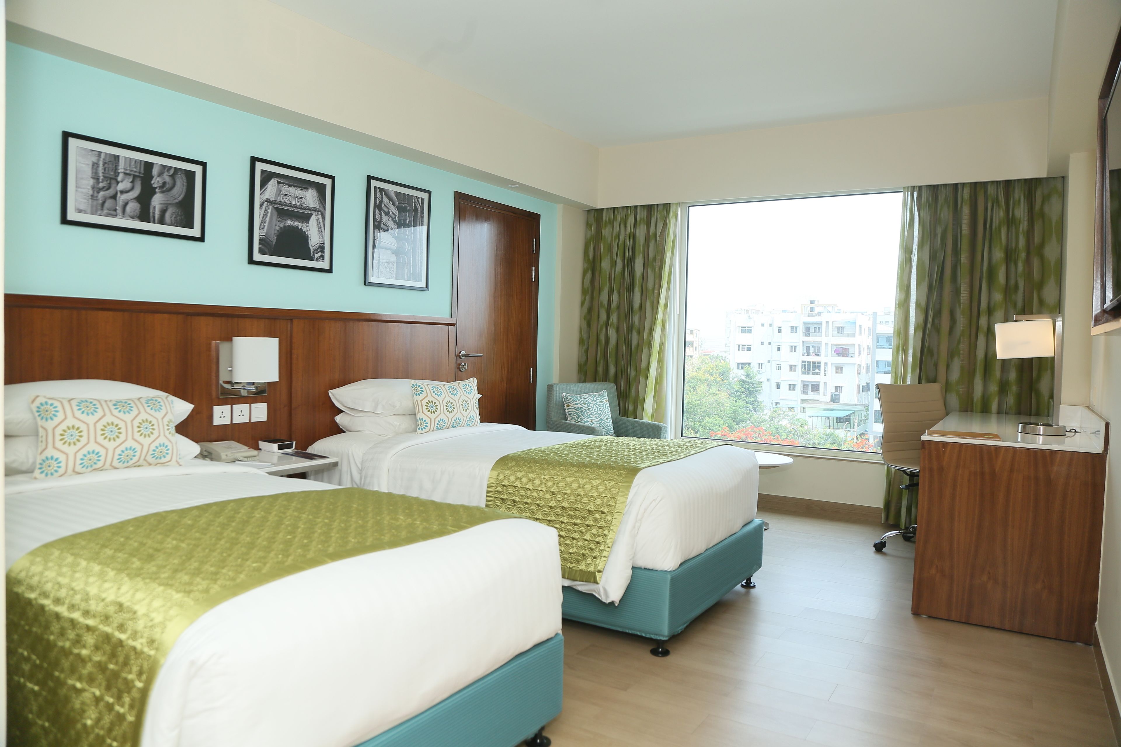 A hotel room with two beds, a desk, a chair, and a large window with curtains.