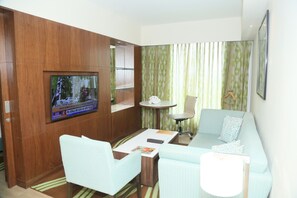 A living room with a television, a sofa, a coffee table, and a small table with a clock. - Fairfield by Marriott Visakapatnam (Visakhapatnam)