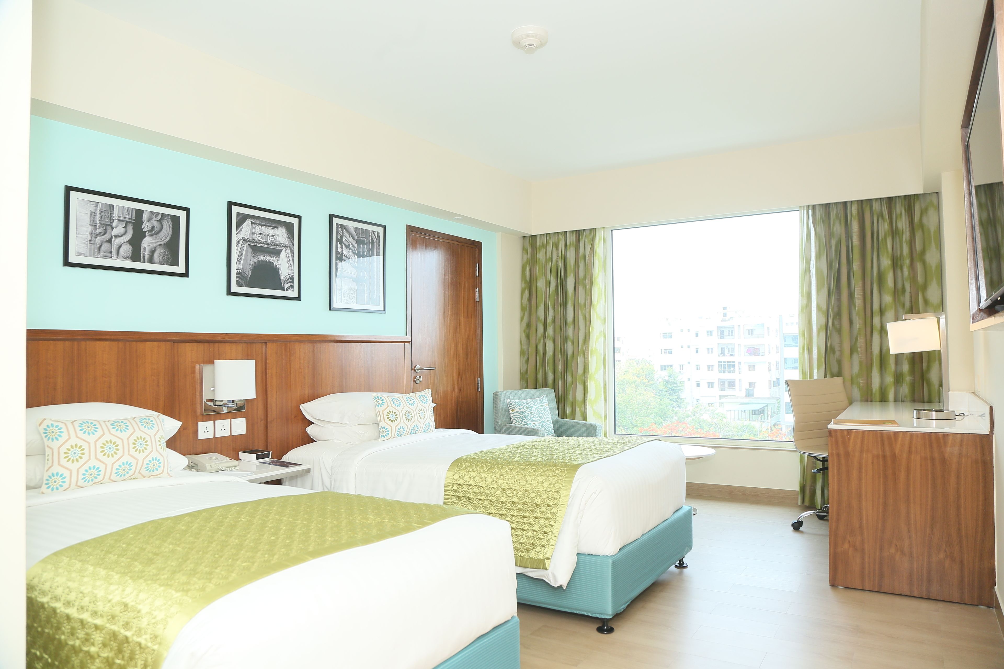 A hotel room with two beds, a desk, a chair, a TV, and a window with curtains.
