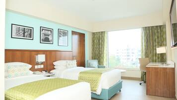 A hotel room with two beds, a desk, a chair, a TV, and a window with curtains.