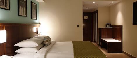 A hotel room with a bed, bedside table, lamp, and a desk with a phone and papers.