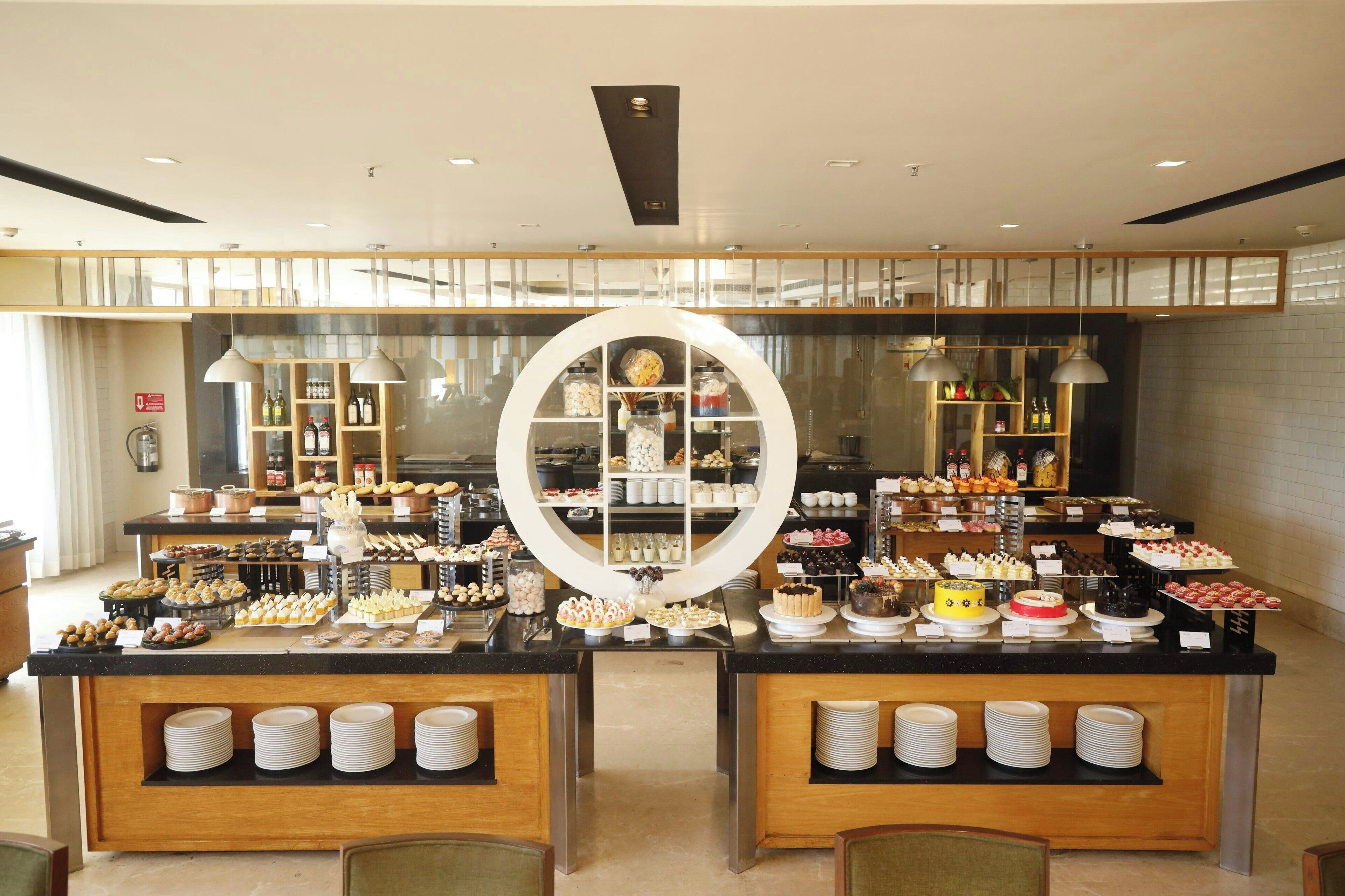 A buffet area with multiple serving stations, a central decorative mirror, and a variety of food and drink options.