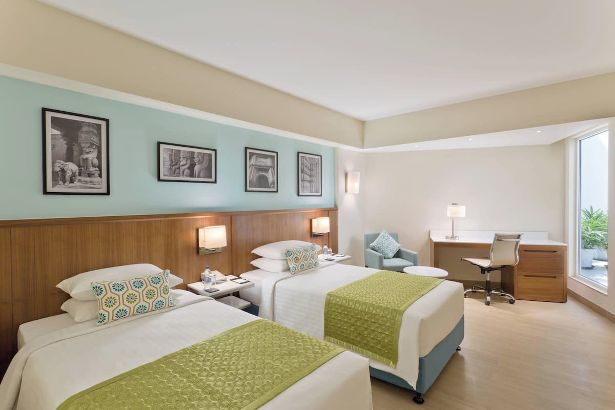 A hotel room with two beds, a desk, a chair, and a large window.