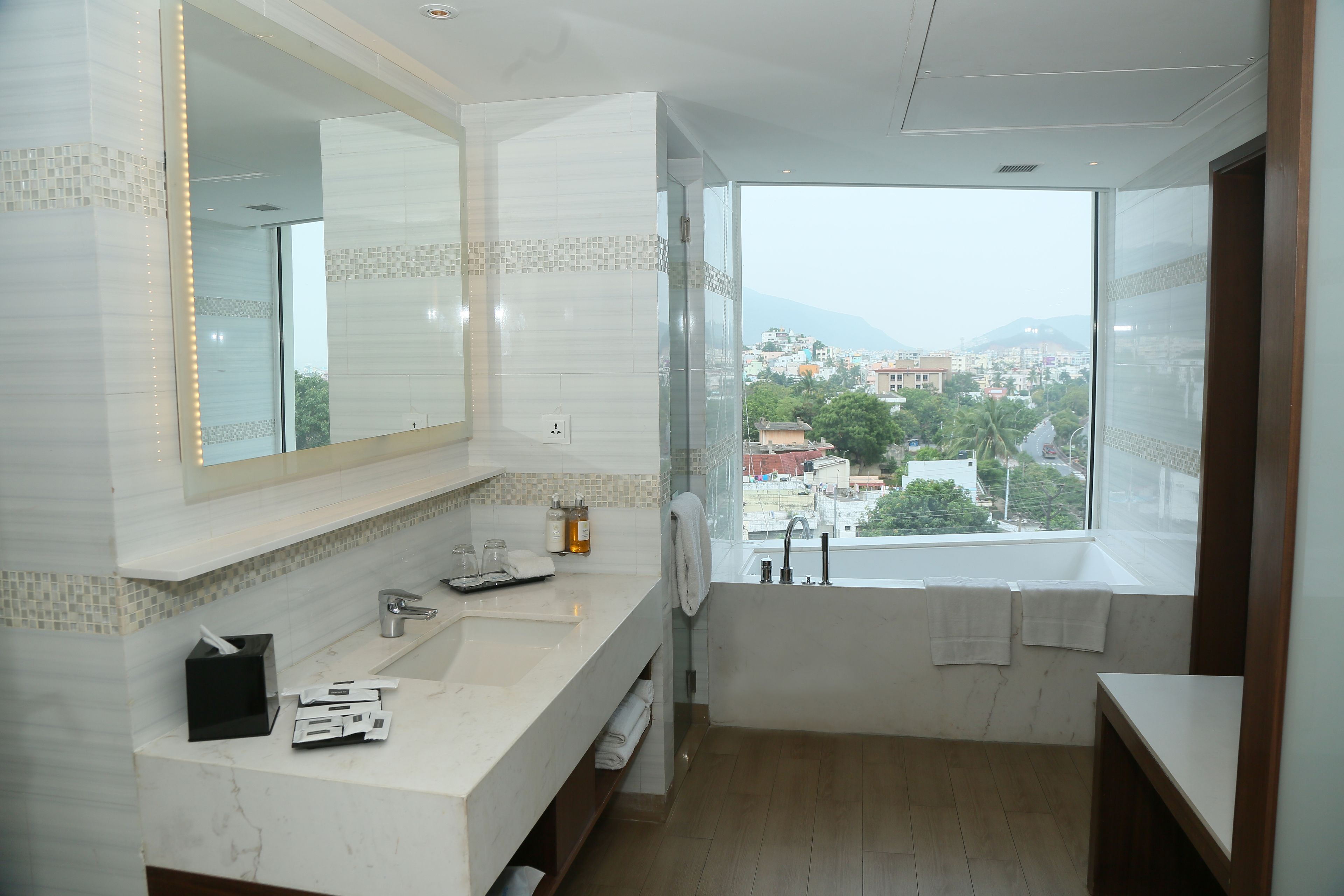 A modern bathroom with a large mirror, white marble countertop, and a bathtub.