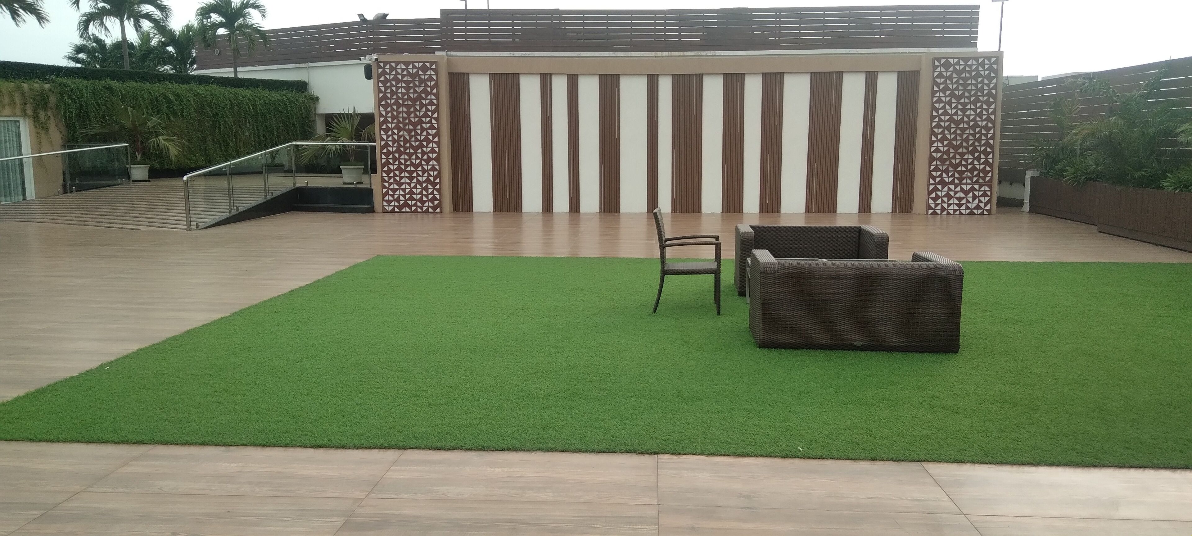 A modern outdoor area with a green artificial turf, a wicker sofa, and a chair.