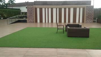A modern outdoor area with a green artificial turf, a wicker sofa, and a chair.