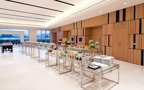 A modern hotel buffet with multiple serving stations, a large window with a view, and wooden paneling on the walls. - Fairfield by Marriott Visakapatnam (Visakhapatnam)