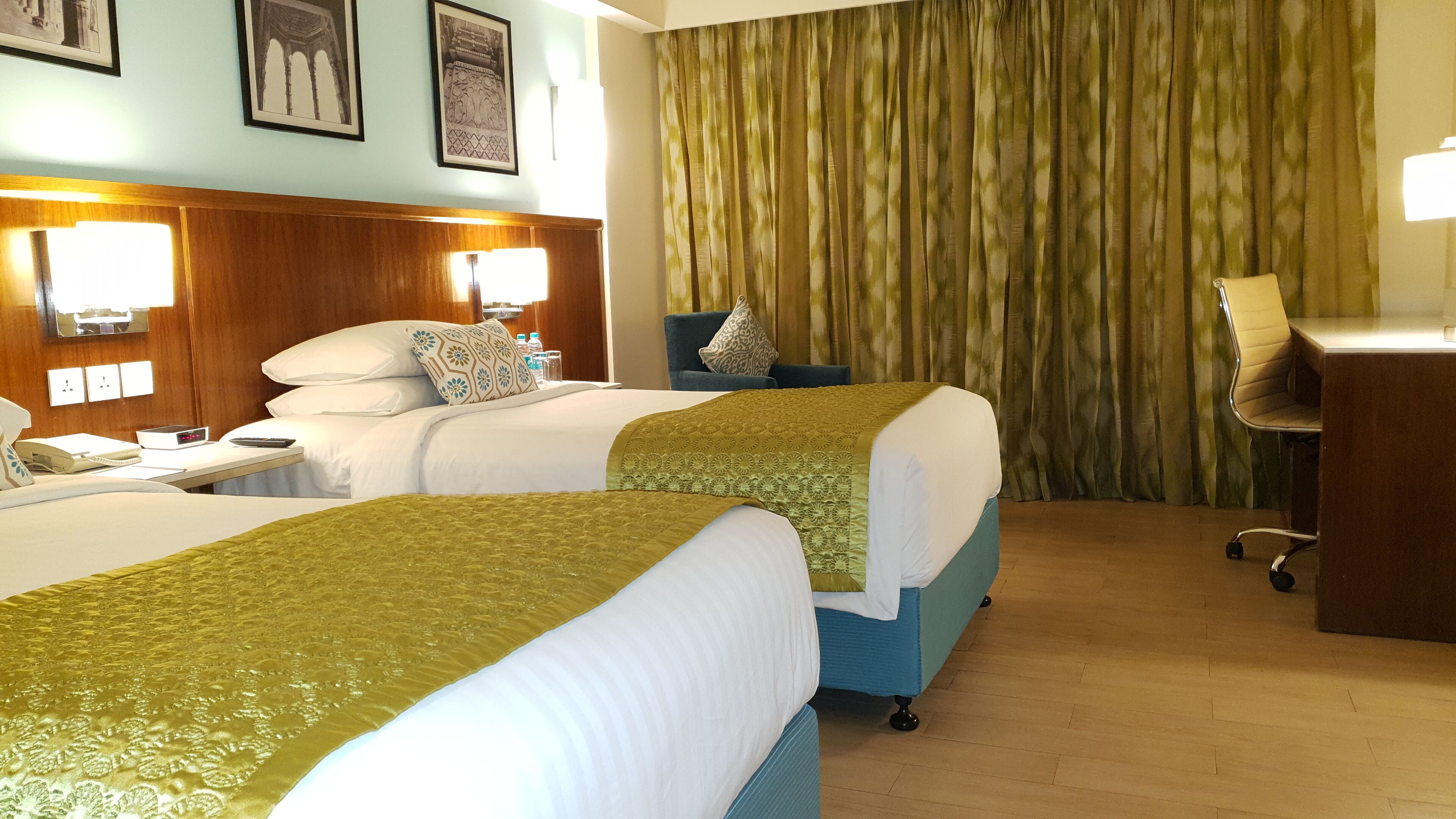A hotel room with two beds, a desk, a chair, and a large window with curtains.