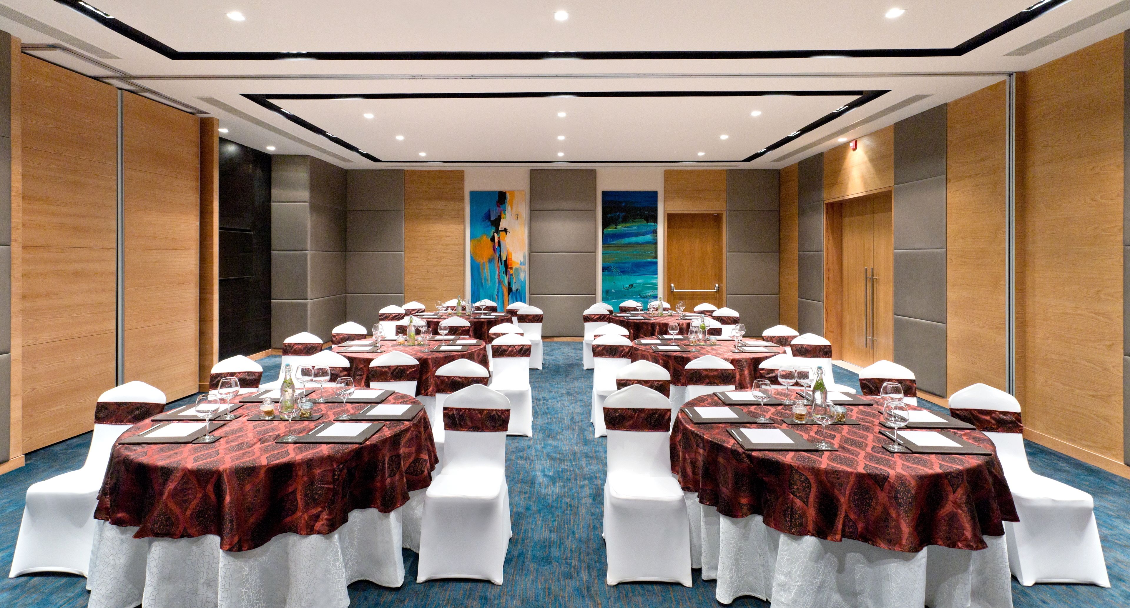 A conference room with multiple round tables, white chairs, and red tablecloths.