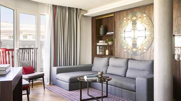 Una sala de estar moderna con un sofá gris, una mesita redonda, una silla roja y una estantería con libros y objetos decorativos.