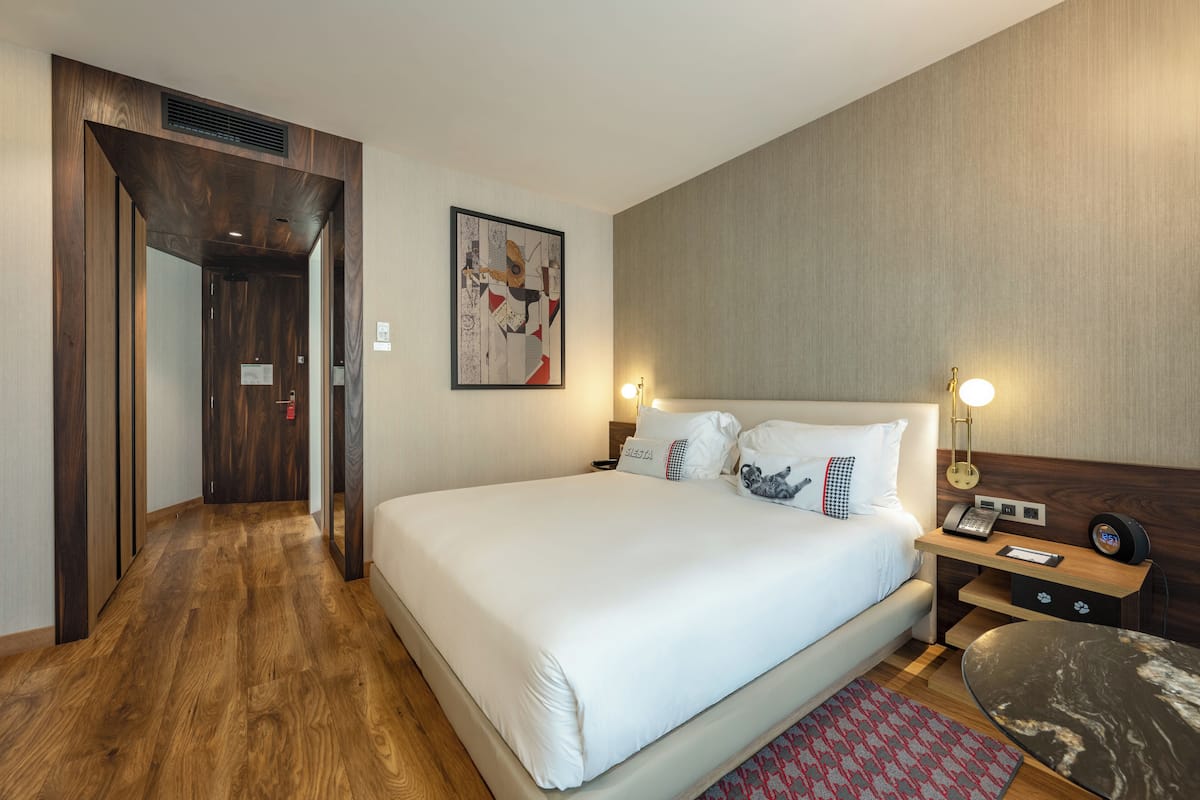 Camera d'albergo con un letto grande, un comodino con una lampada, un'opera d'arte appesa al muro e un pavimento in legno.