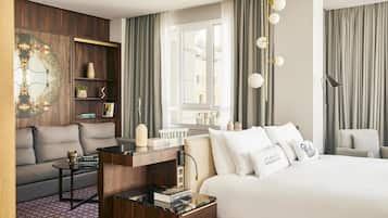 Una habitación de hotel moderna con una cama grande, un sofá, una mesita, una estantería y una ventana con cortinas.
