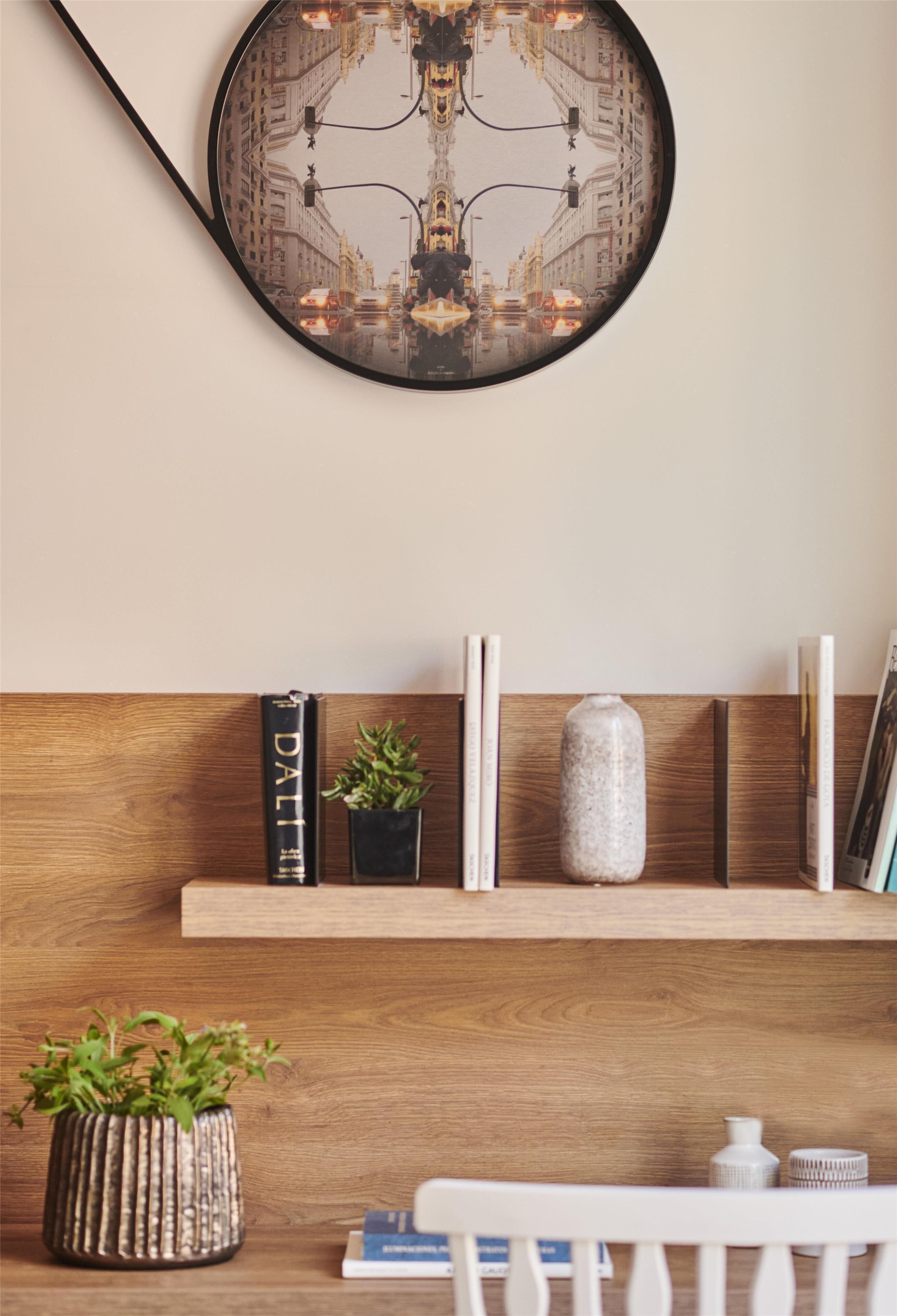 A wall-mounted mirror reflecting a street scene, a wooden shelf with books and decorative items, and a white chair in the foreground.
