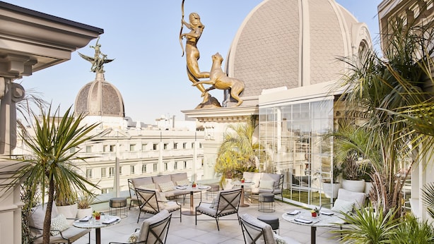 Una terraza en la azotea con mobiliario exterior, una estatua y vistas de la ciudad.