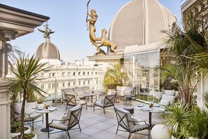 A rooftop terrace with outdoor seating, a statue, and a view of the cityscape.