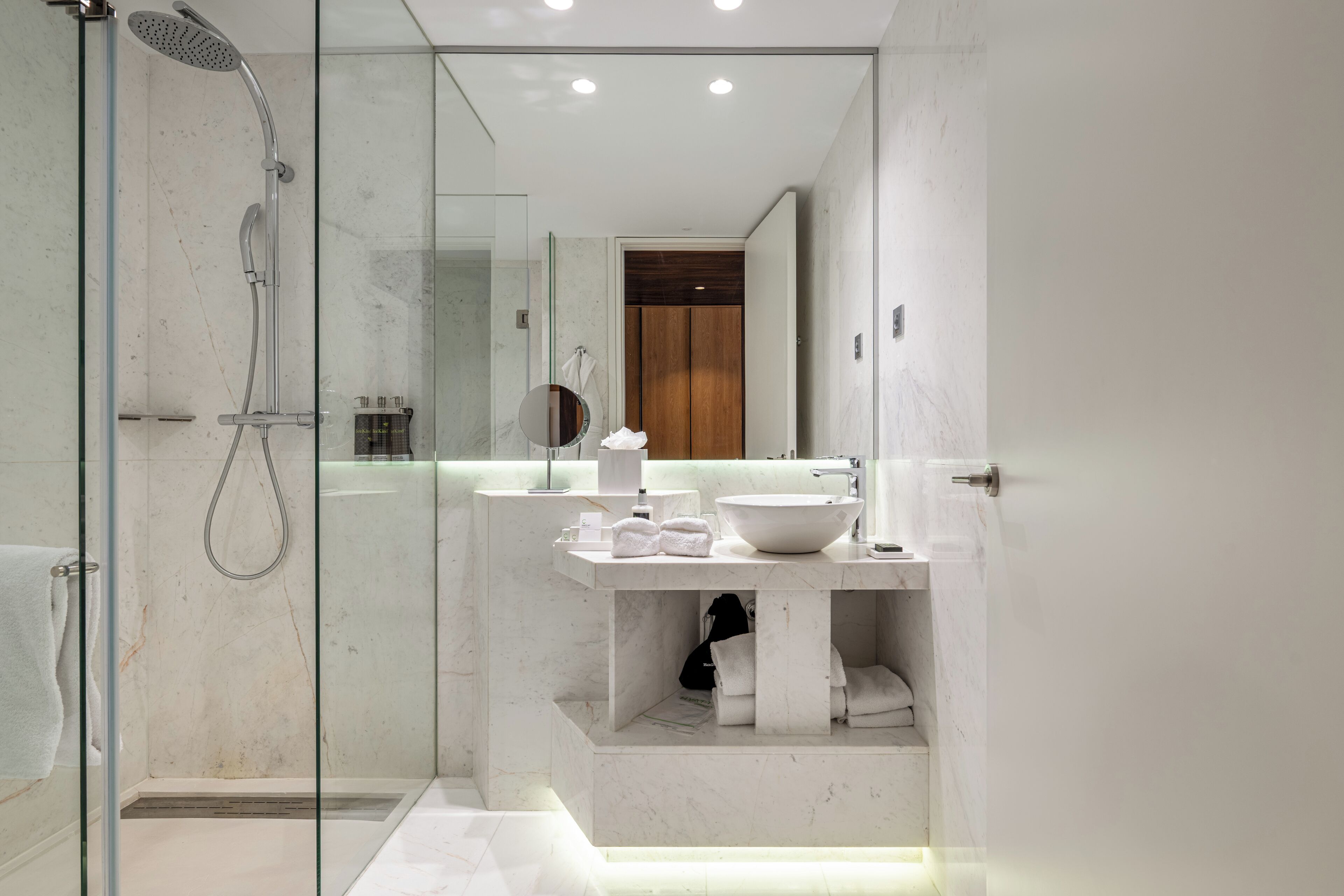 Un baño moderno con cabina de ducha de vidrio, lavamanos de mármol y puerta de madera.
