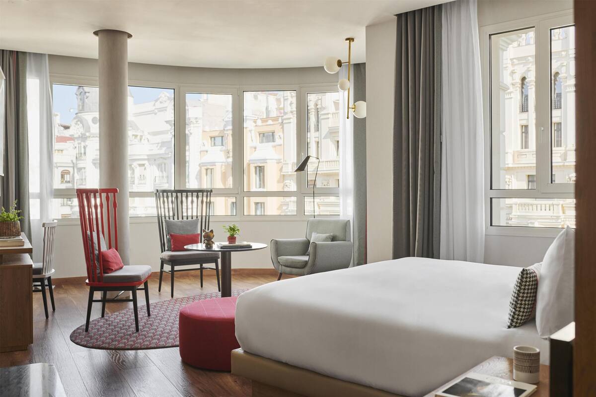 Una camera d'albergo con un letto grande, due poltrone, un tavolino e ampie finestre con vista sulla città.