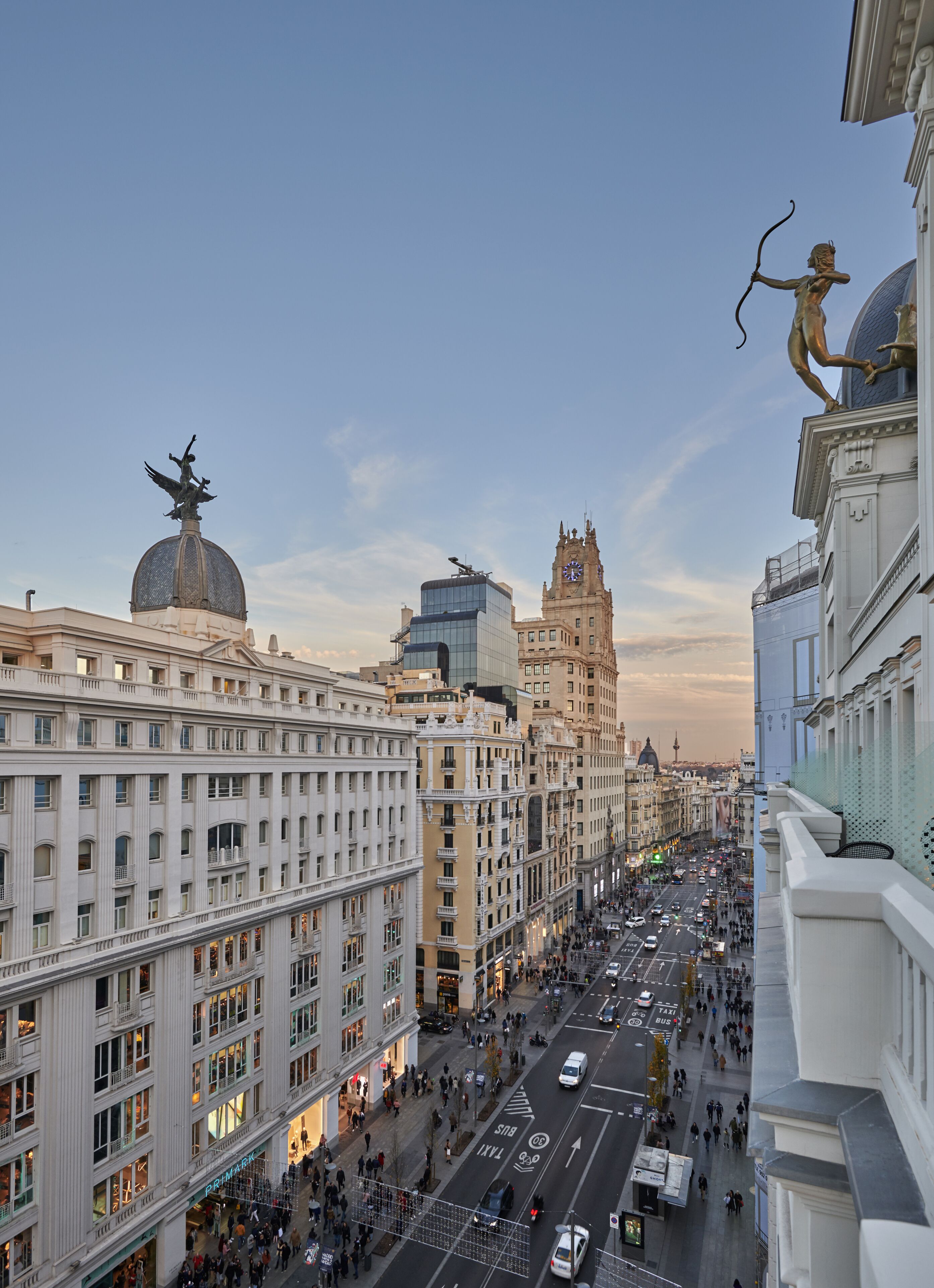 Paesaggio urbano con edifici storici, una torre dell'orologio in evidenza e una statua all'angolo di un palazzo.