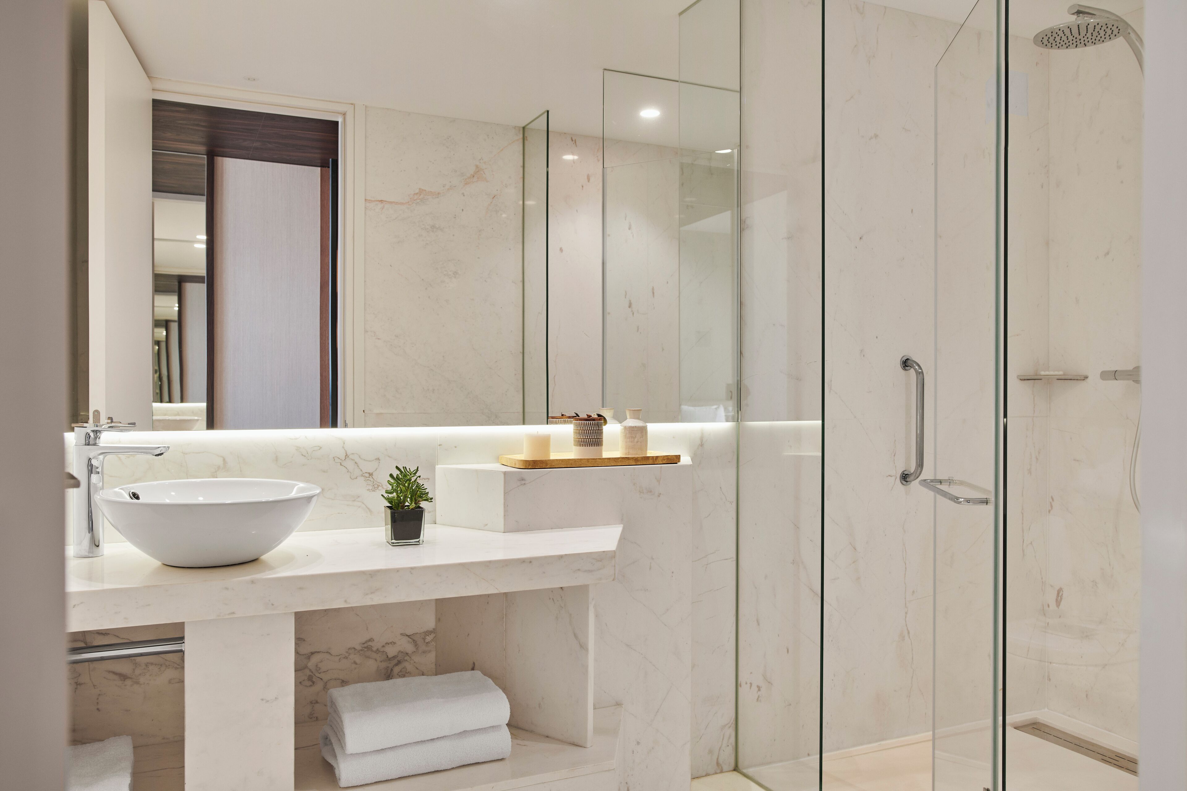 A modern bathroom with a white marble sink, a glass shower enclosure, and a large mirror.