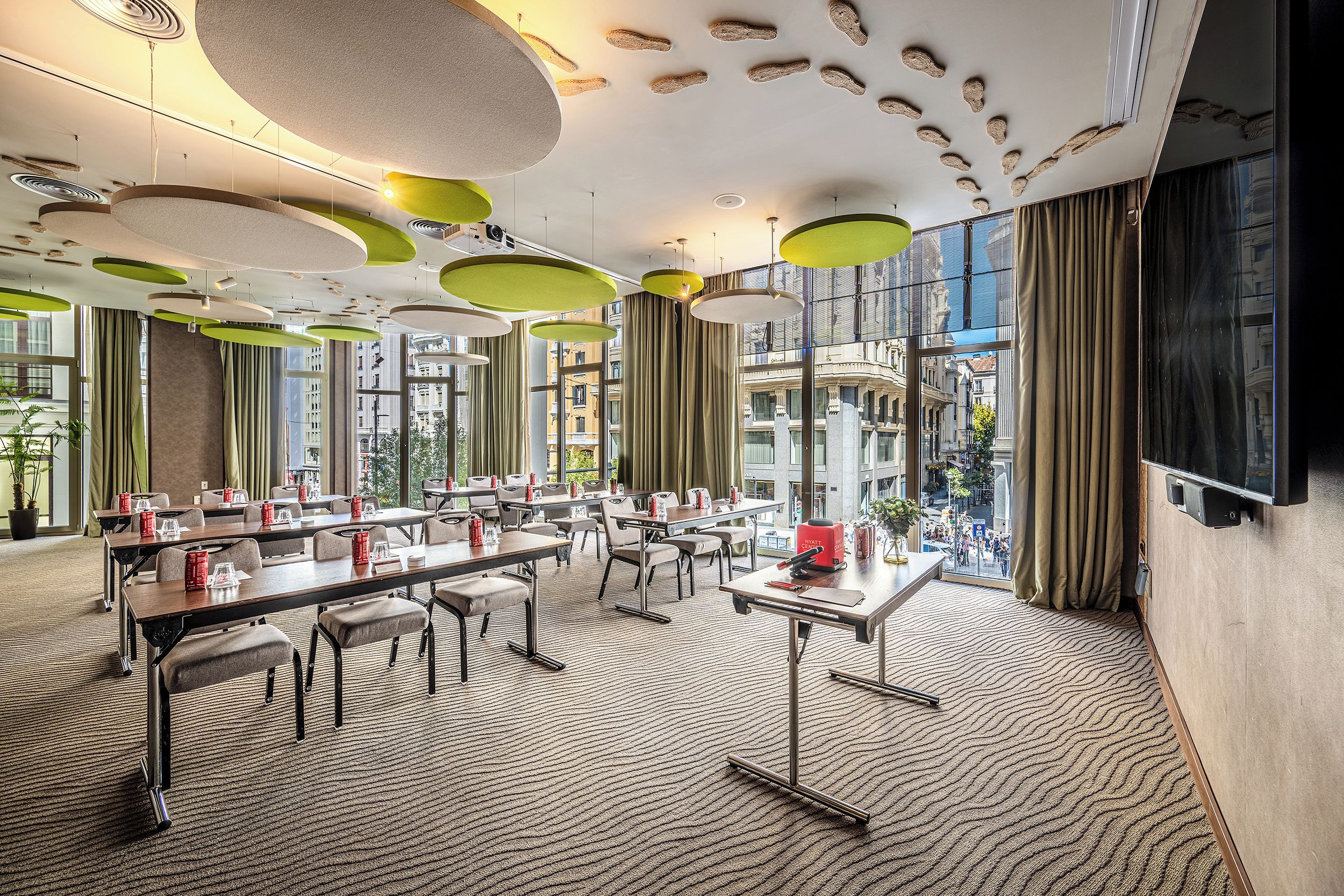 Une salle de conférence d’hôtel équipée de tables, de chaises et d’une grande fenêtre donnant sur la ville.
