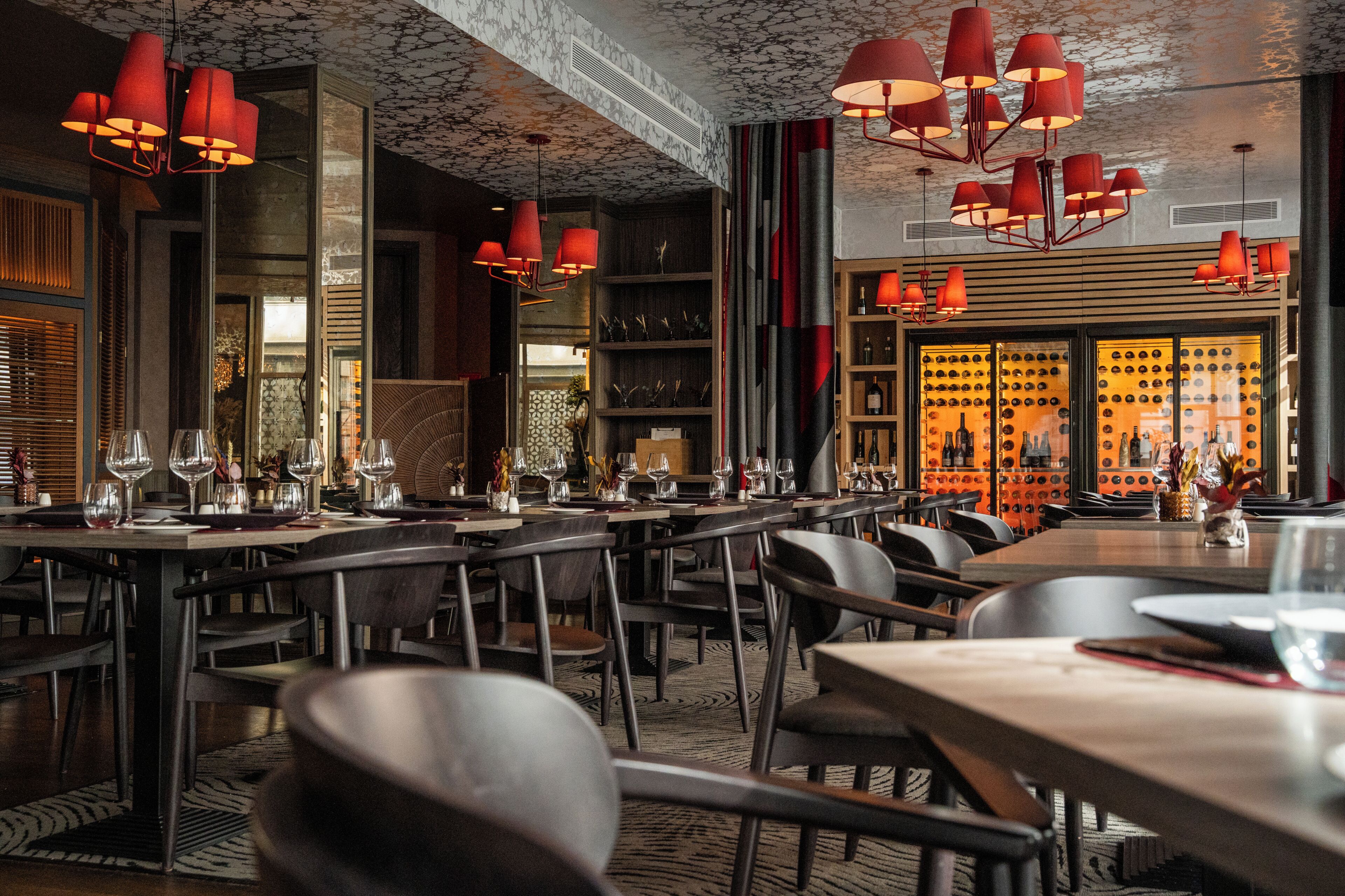 Een restaurantinterieur met meerdere tafels, stoelen en rode hanglampen.