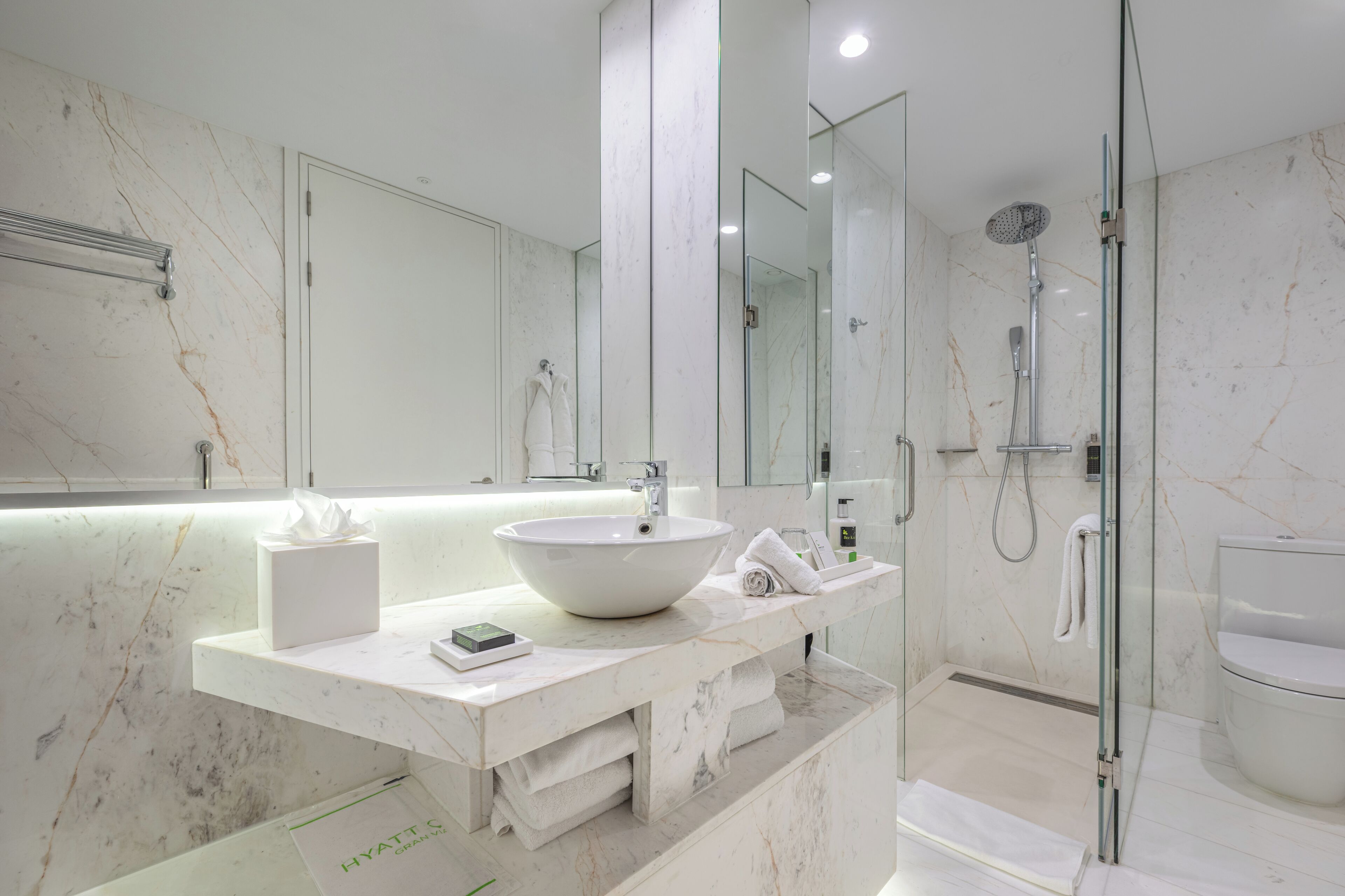 A modern bathroom with a large white sink, a glass-enclosed shower, and a marble-tiled wall.