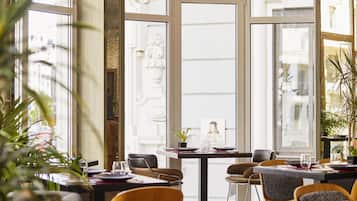 Een restaurantinterieur met grote ramen, tafels, stoelen en potplanten.