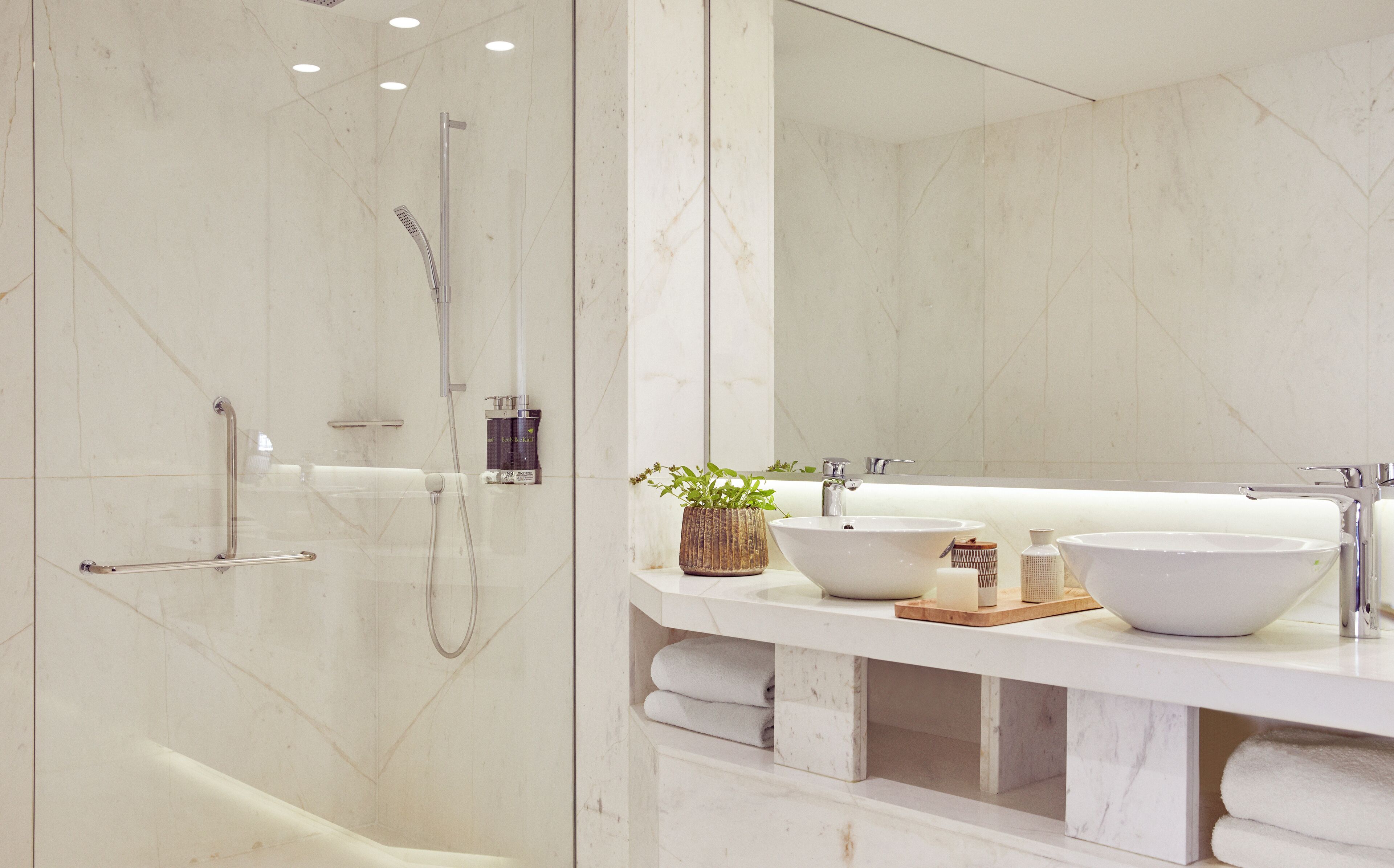 Une salle de bain moderne avec une douche à parois de verre, deux lavabos et un grand miroir.