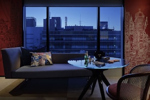 A modern room with a glass table, a sofa with patterned cushions, and a view of city buildings through large windows.
