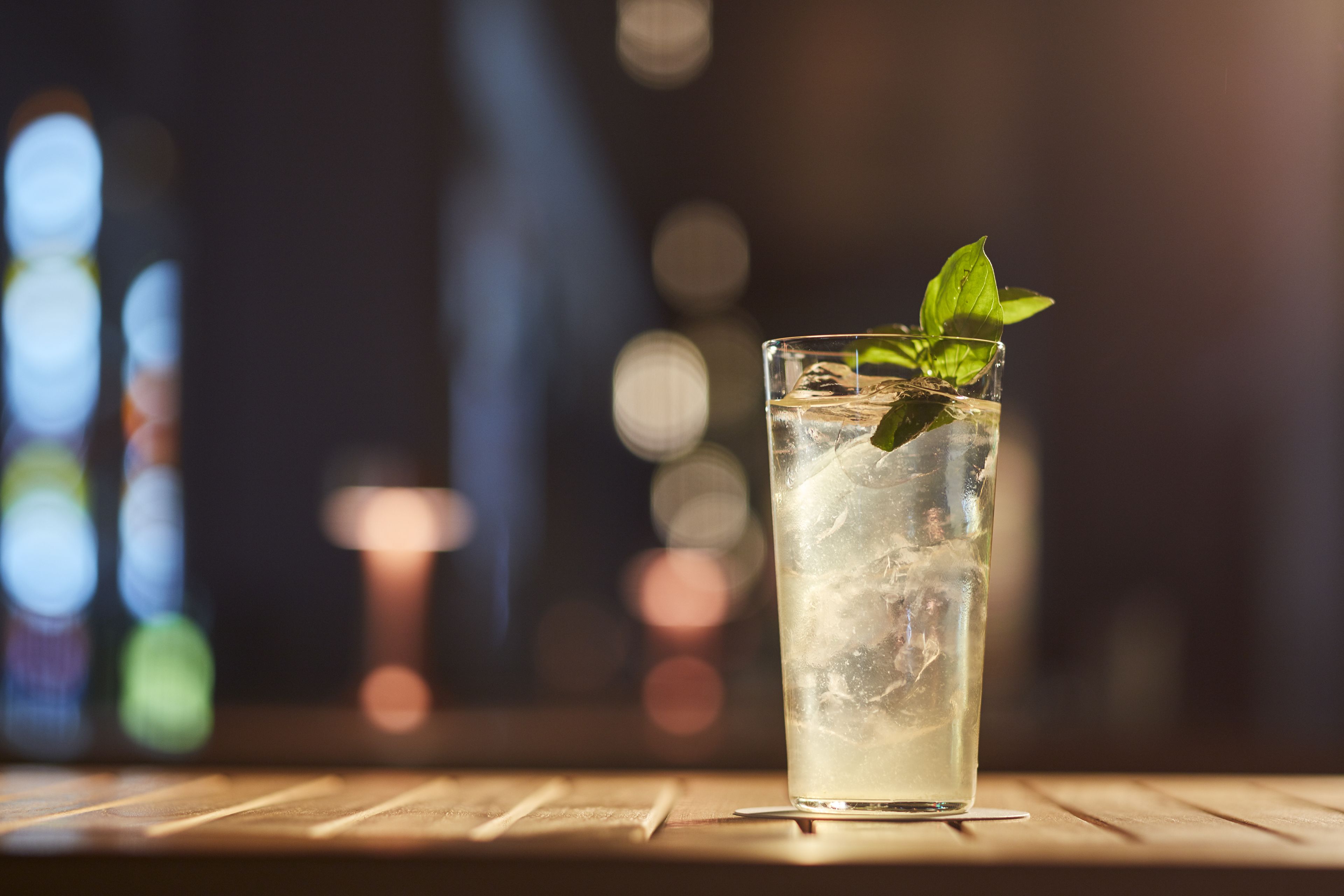 A glass of iced beverage with mint leaves on a wooden surface.