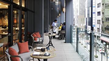 Ein Café im Innenbereich mit Tischen und Stühlen, Blick auf die Straße und eine Person im Hintergrund.