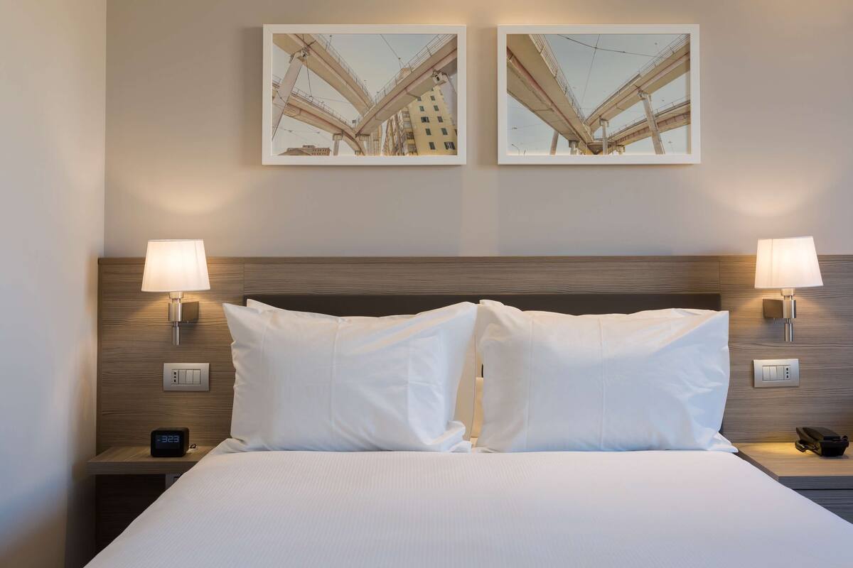 A hotel room with a large bed, two wall-mounted lamps, a nightstand with a phone, and two framed pictures on the wall.