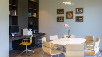 A modern meeting room with a round table, six chairs, a computer, and shelves with books and decorative items.