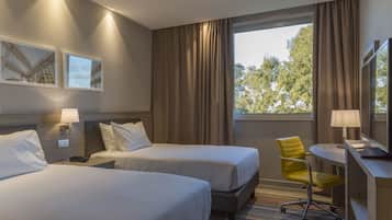 A hotel room with two beds, a desk, a chair, and a window with curtains.