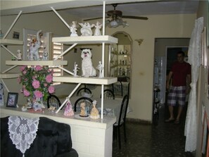 Ein Zimmer mit einer weißen Regaleinrichtung, die verschiedene Figuren zeigt, und einem Tisch mit weißer Spitzenleinentuch.
