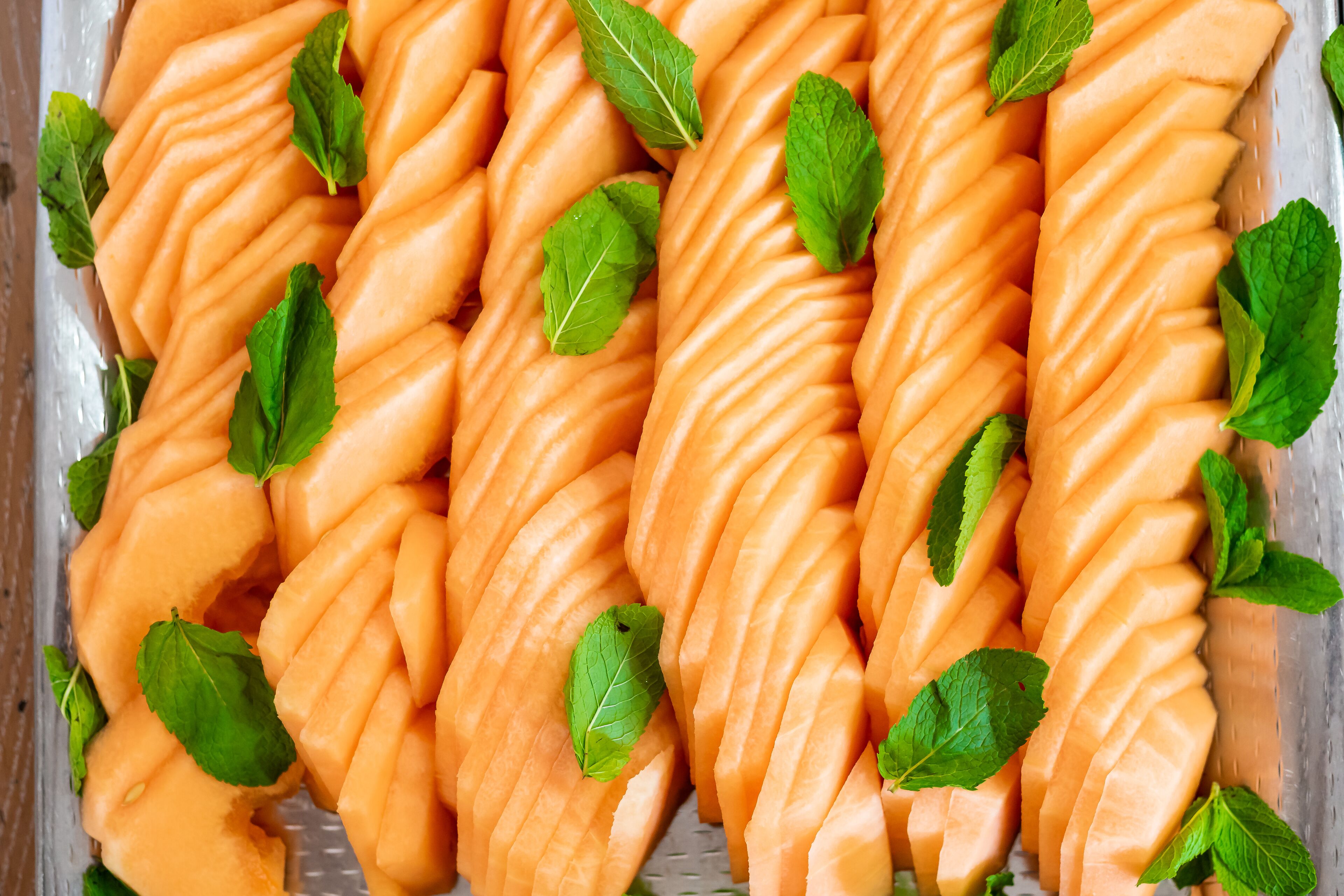 A tray of neatly arranged cantaloupe wedges garnished with mint leaves.