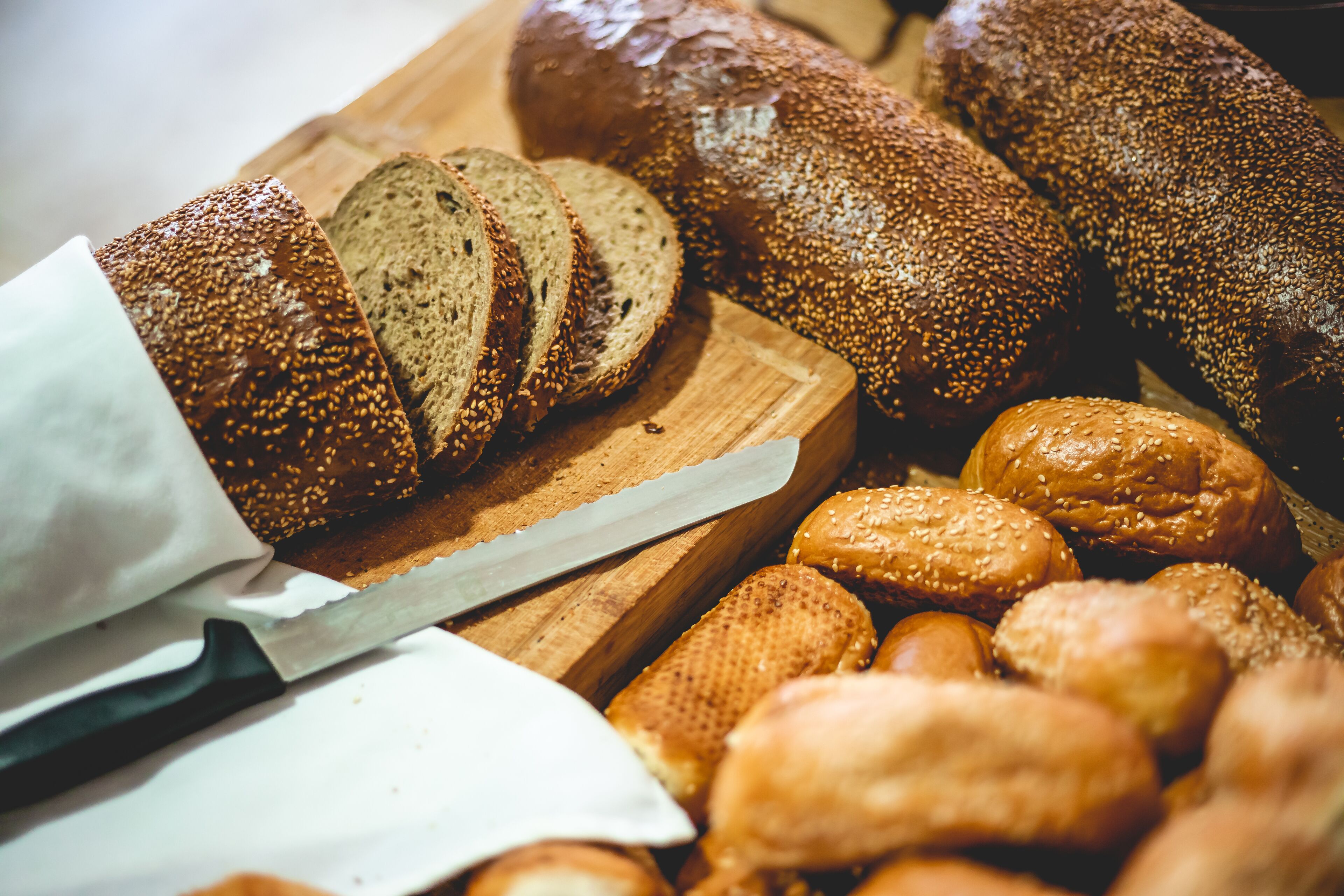 A variety of breads on a wooden cutting board, including sliced loaves and rolls.