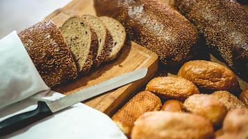 A variety of breads on a wooden cutting board, including sliced loaves and rolls.
