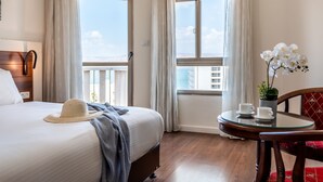 A hotel room with a bed, a small table with cups, a chair, and a balcony with a view of the ocean. - Aviv Holiday Flat (Tiberias)