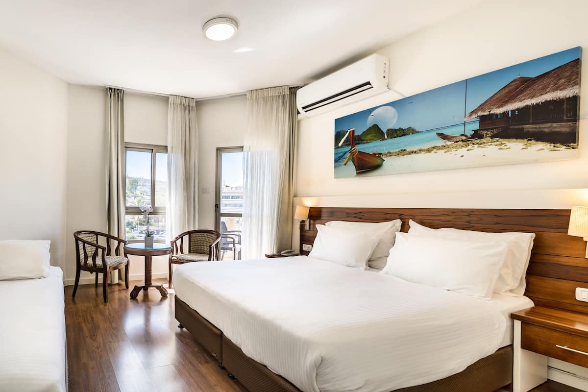 A hotel room with two beds, a dining table, chairs, a large window, and artwork on the walls.