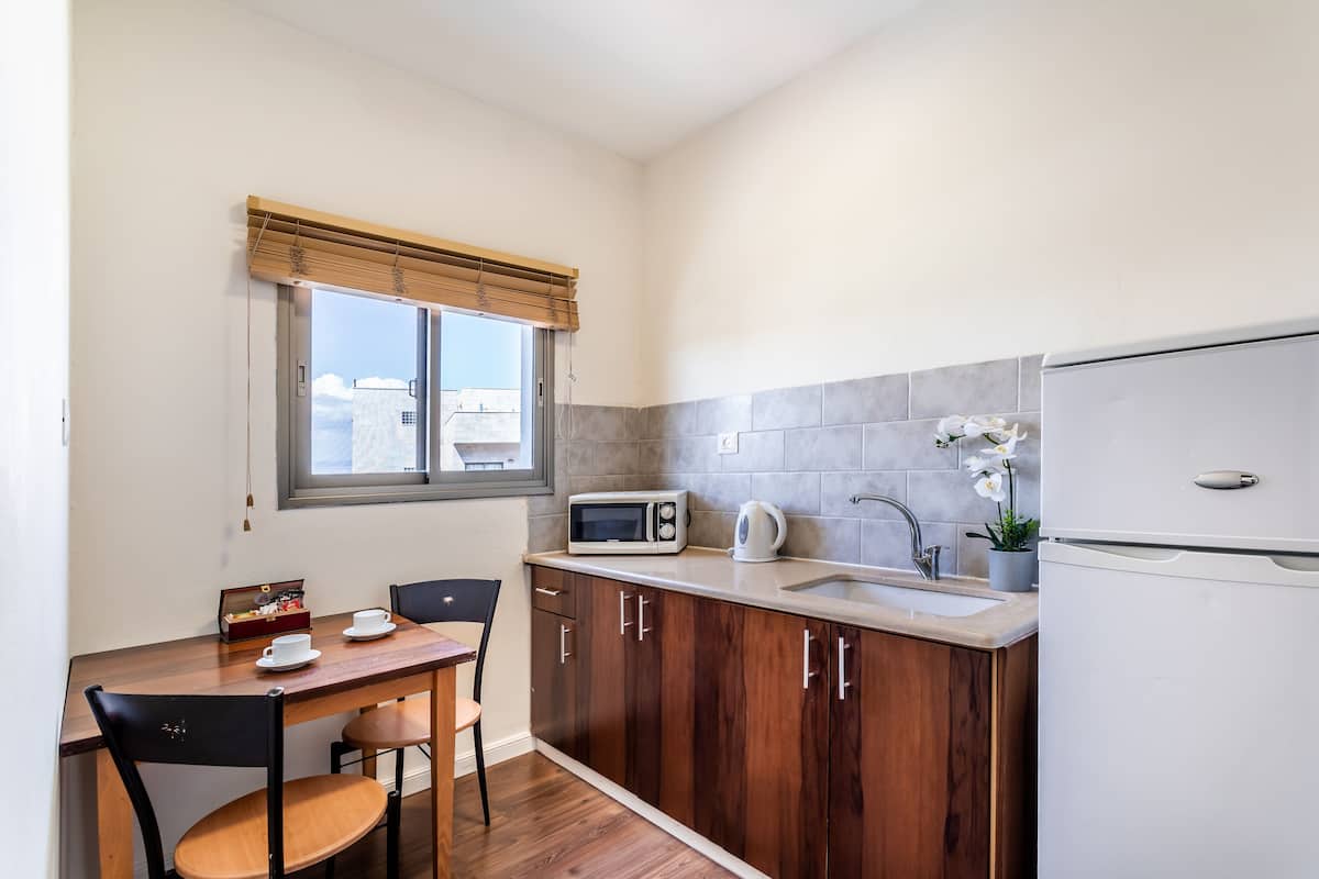 A compact kitchen with wooden cabinets, a microwave, a kettle, a sink, and a refrigerator.