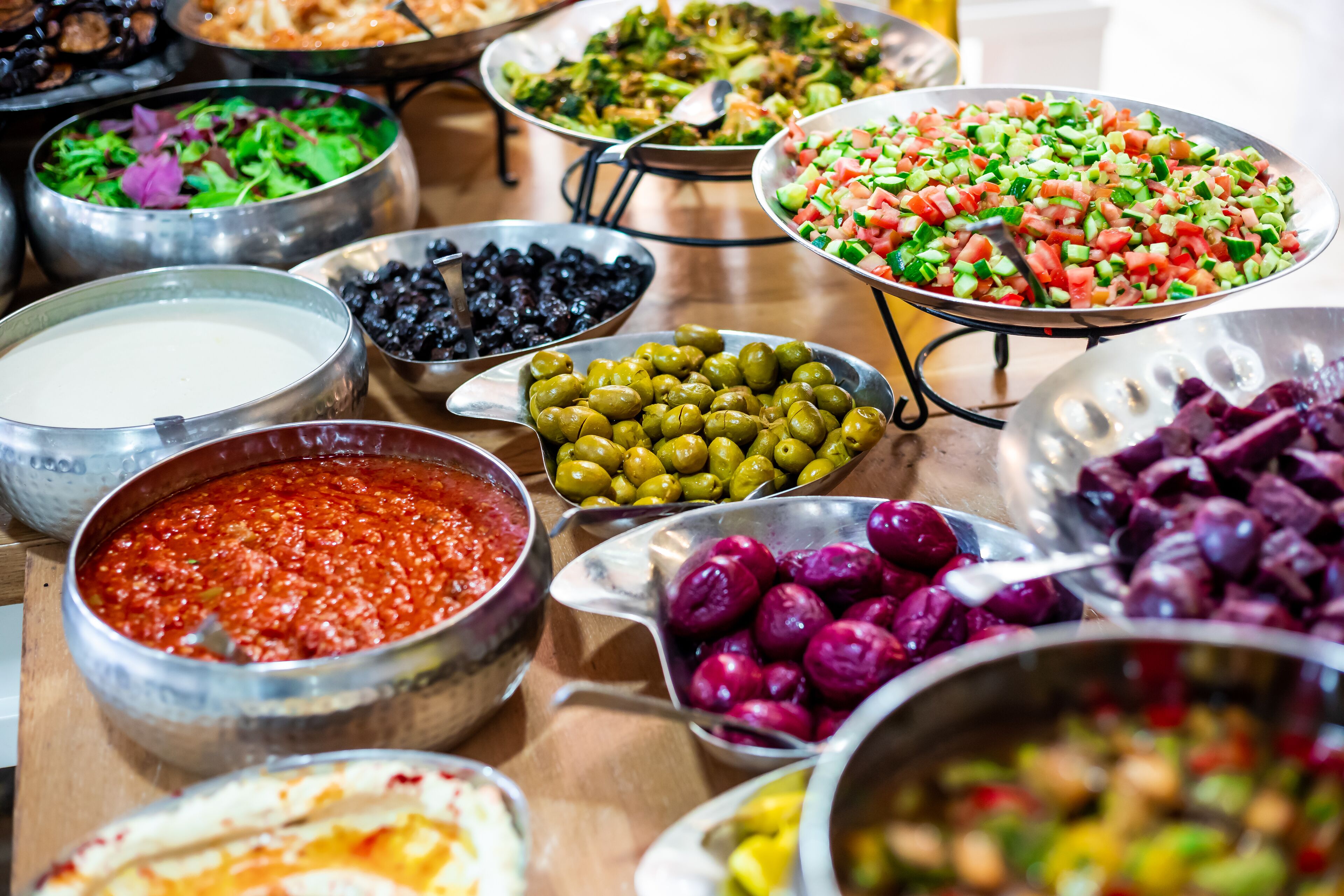 Variedad de alimentos expuestos en una mesa, entre ellos aceitunas y una ensalada.