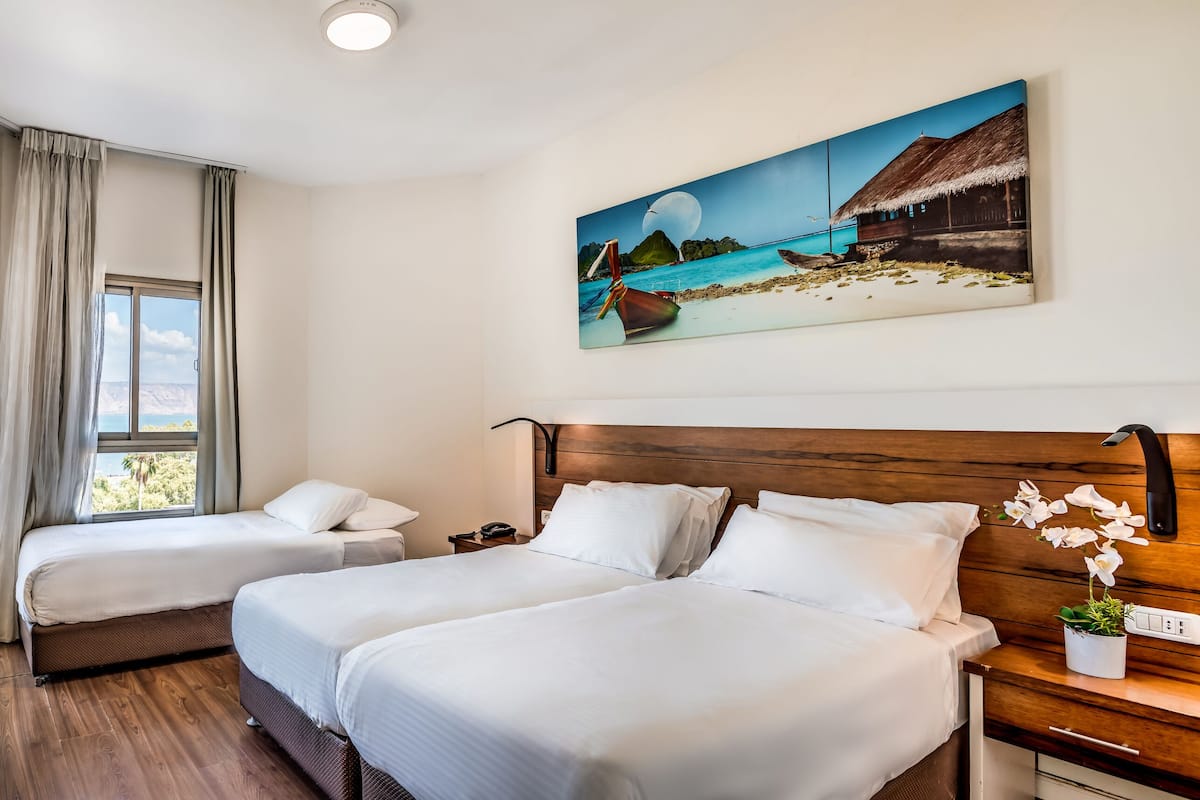 A hotel room with two beds, a TV, a painting of a beach scene, and a potted orchid.