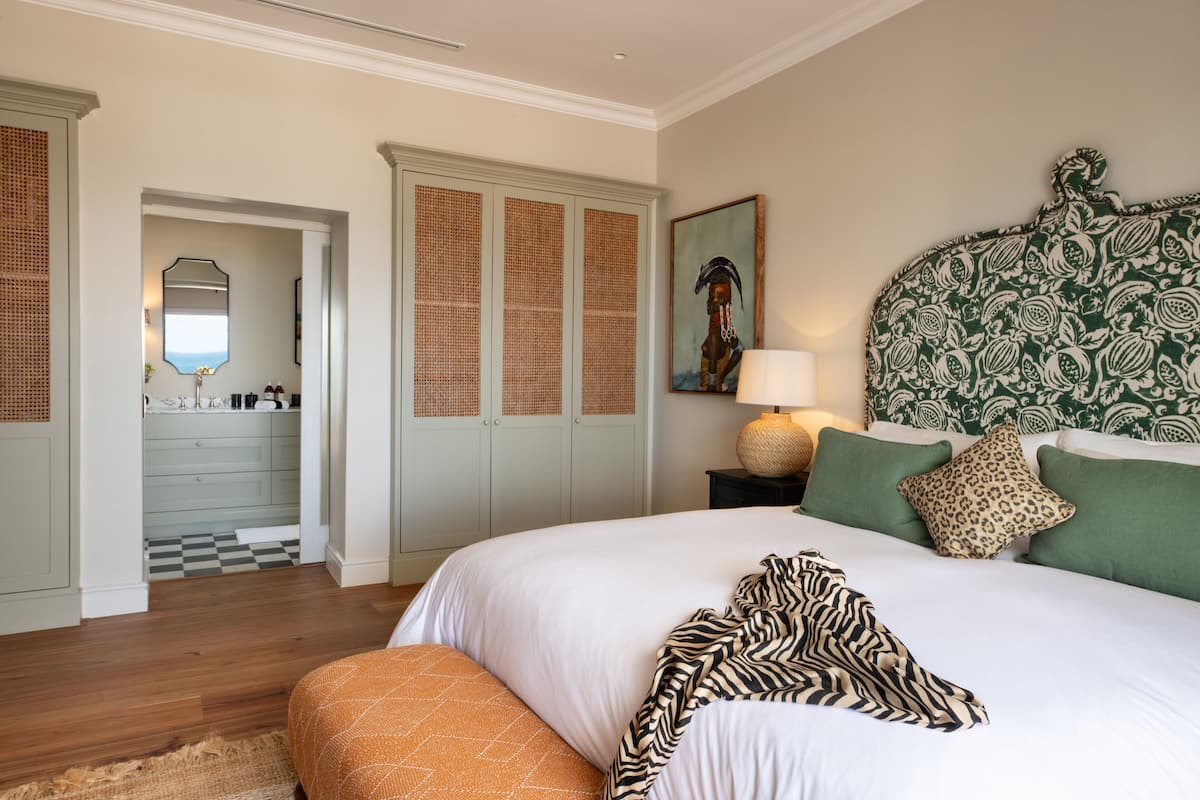 Un dormitorio con una cama grande, un cabecero con estampado verde y blanco, un plaid de estampado de cebra y un piso a cuadros.