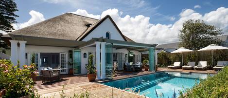 A house with a swimming pool, outdoor furniture, and potted plants.