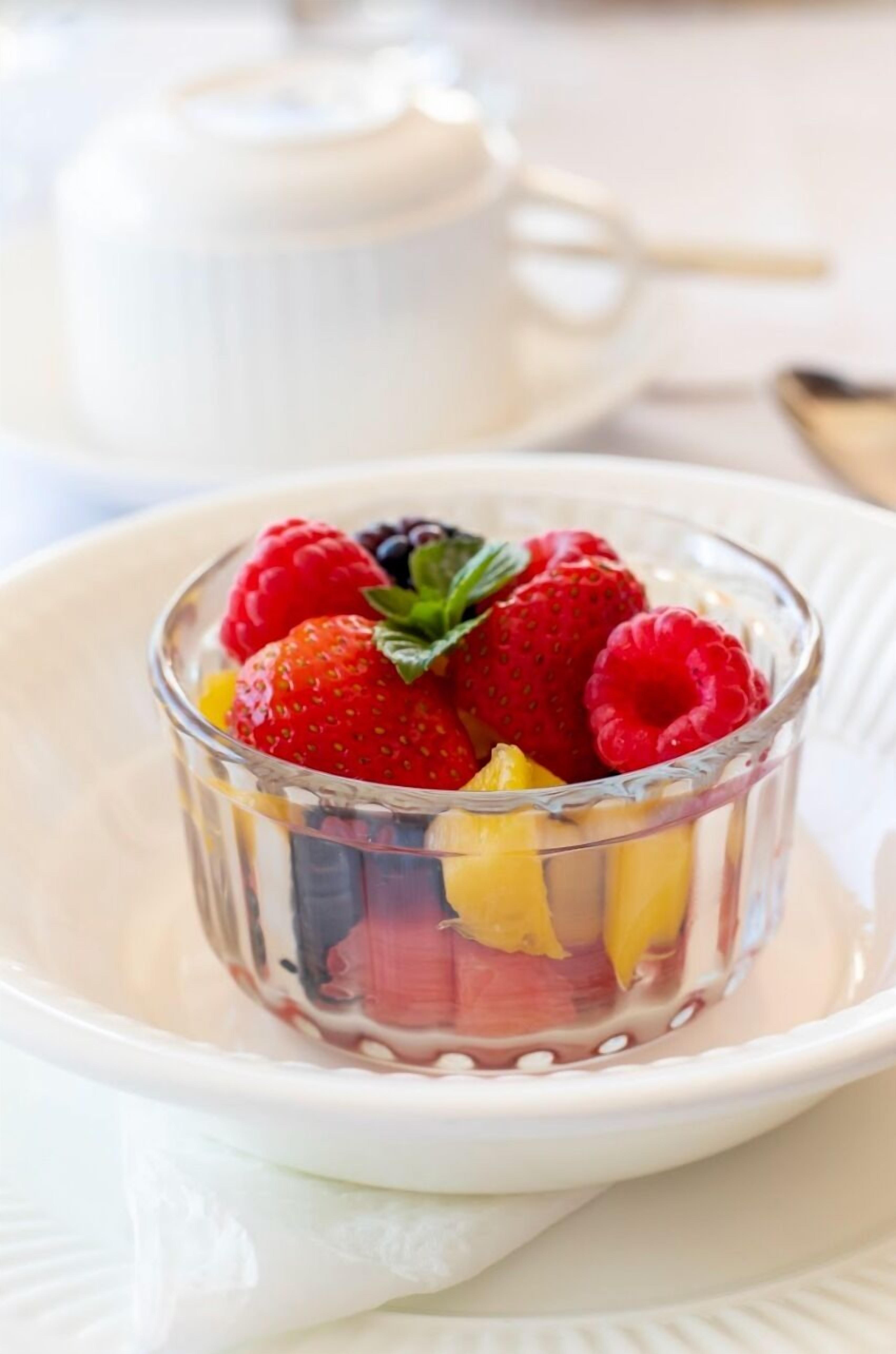 Un dessert servi dans un bol en verre transparent, posé sur une assiette blanche, avec une théière blanche en arrière-plan.