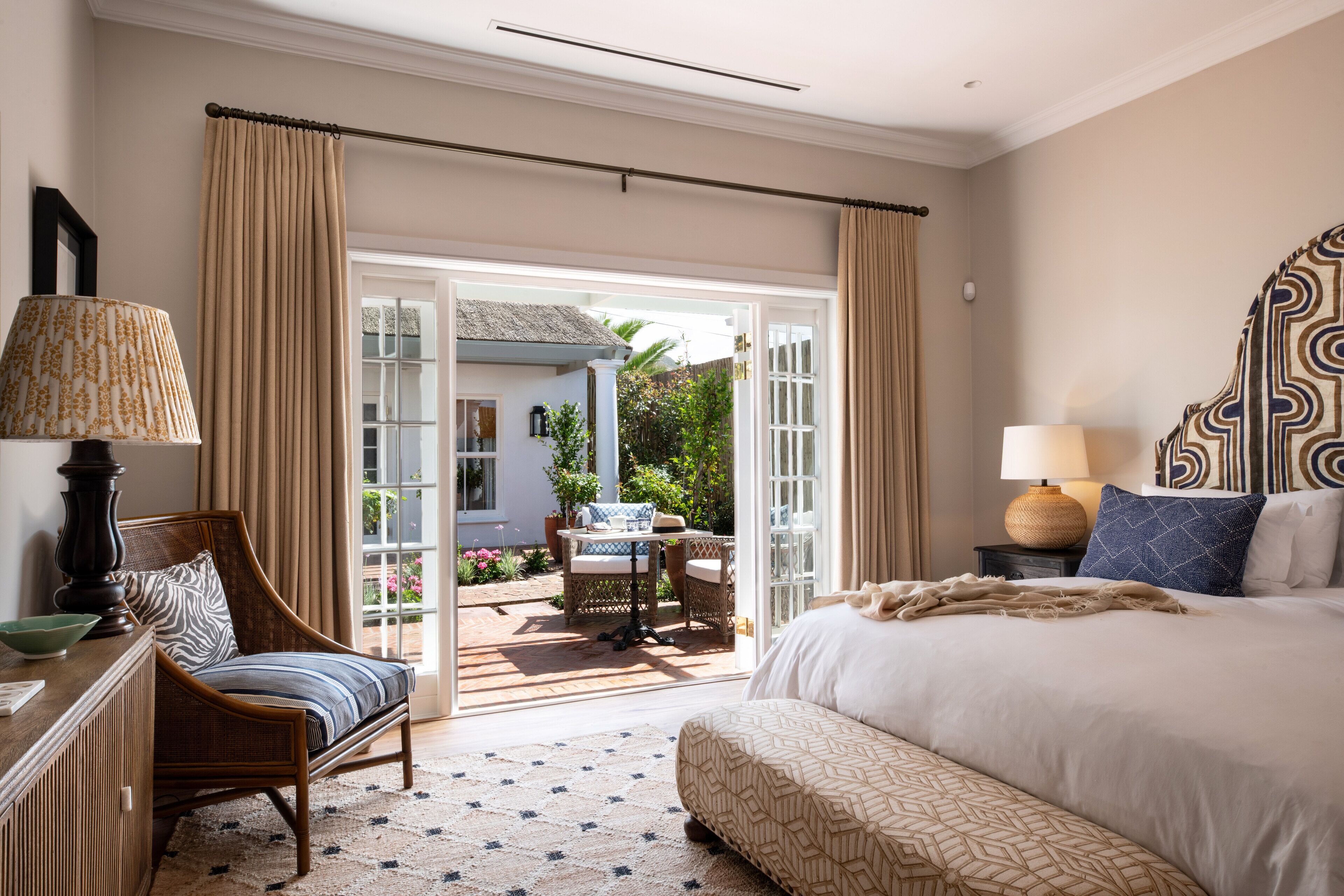 Un dormitorio con una cama grande, una silla, una mesa y vistas a un patio exterior.