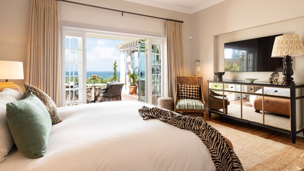 Une chambre spacieuse dotée d’un grand lit, d’une télévision et d’un balcon aménagé avec du mobilier d’extérieur.