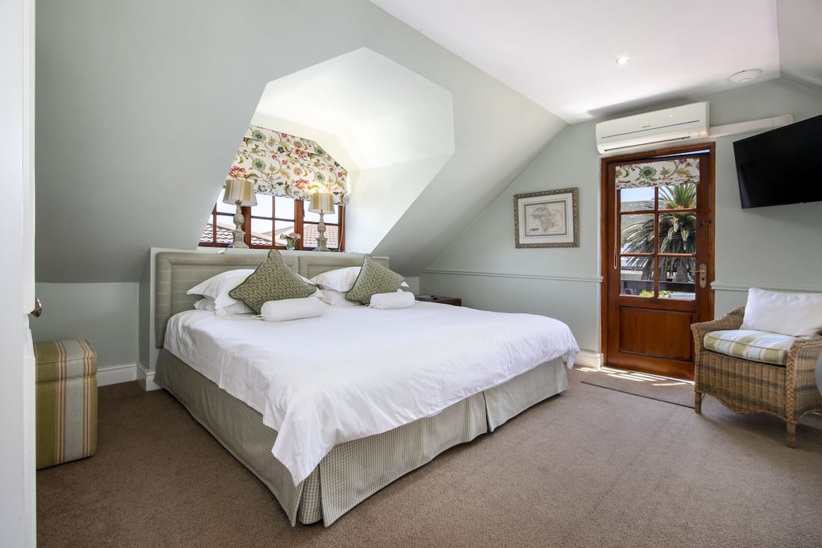 Un dormitorio con una cama grande, una ventana con cortinas florales, una silla de mimbre y una puerta que da al exterior.